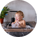 Baby sitter i en vask og ler mens han leker med vann