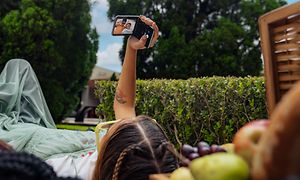 Jente som holder Motorola Razr-telefonen mens hun ligger på plenen med venninnen sin og tar selfie