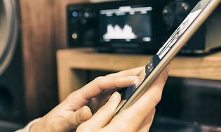 Person streaming music from a tablet with a media player and speaker in the background