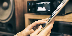 Person streaming music from a tablet with a media player and speaker in the background