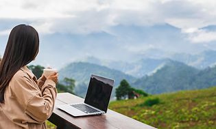 b2b workation - kvinne som ser utover fjellandskap med en kopp kaffe og en laptop