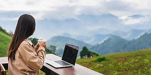 b2b workation - kvinne som ser utover fjellandskap med en kopp kaffe og en laptop