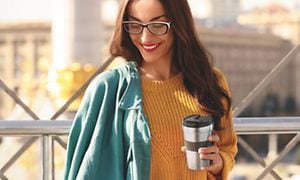 Kvinne med en kaffe på farten i en Delongi-termokopp
