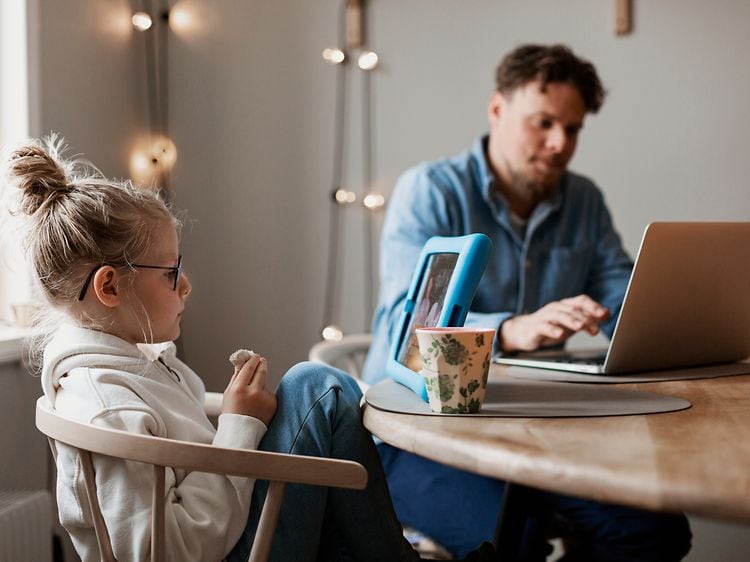 Far og datter bruker bærbar PC og nettbrett ved spisebord