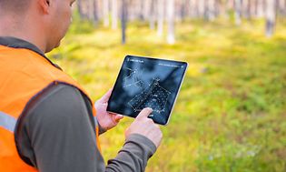 Mann sjekker planer på nettbrettet sitt i skogen