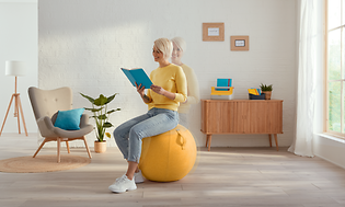 Kvinne som leser bok mens hun sitter på gul sitteball