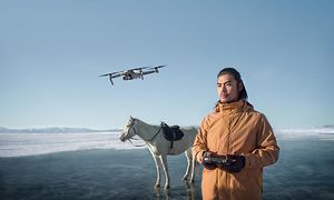 Mann flyr drone over is med hest i bakgrunnen