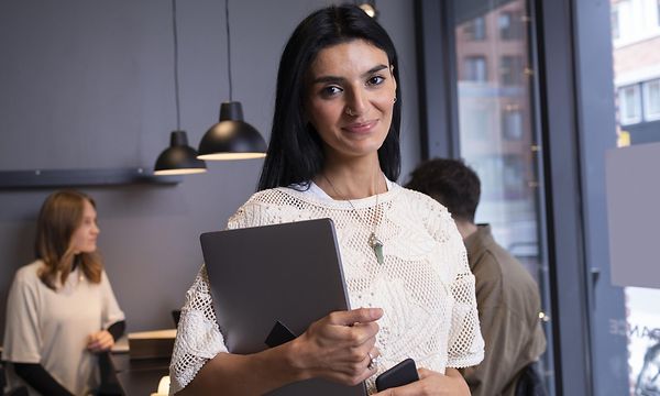 Smilende kvinne holder et nettbrett i armene sine på kontoret