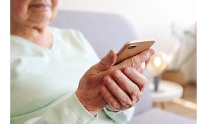 Eldre kvinne sitter med telefonen i hånda