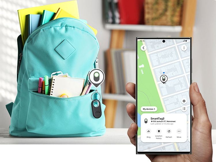 Sort Samsung SmartTag2 på en ryggsekk og en hånd som holder en smarttelefon med app-en for å finne den