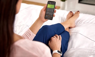 Smarttelefon som viser Garmin Connect-appen i hånden på en dame som sitter i sengen