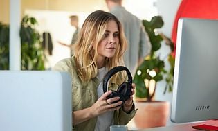 Woman working with PC using Microsoft 365 Office and holding headset in her hands