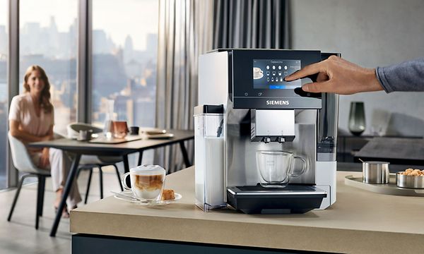 Siemens EQ700 kaffemaskin på benkeplate med kvinne i bakgrunnen