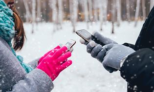 To personer med hver sin mobil ute i snøen