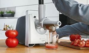 Person lager fersk tomatjuice med fruktpresseren til Bosch-kjøttkverner