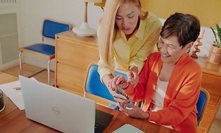 To damer foran en bærbar PC og en smarttelefon