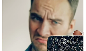mann holder smarttelefon med knust skjerm og ser misfornøyd ut
