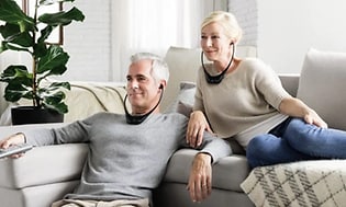 Mann og kvinne slapper av i sofaen mens de ser TV med hodetelefoner