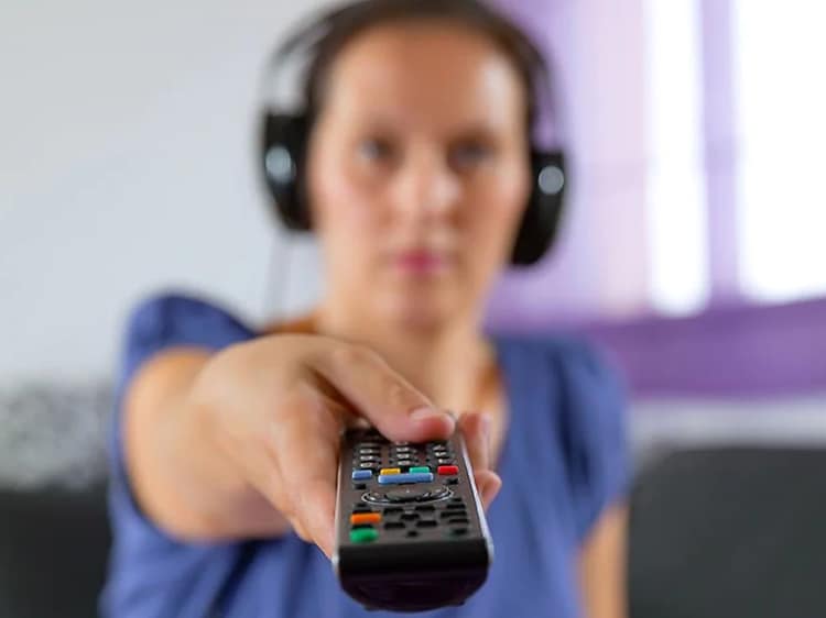 Kvinne med trådløse hodetelefoner peker fjernkontrollen mot TV-en