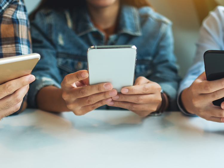 tre ungdommer bruker smarttelefon ved et bord