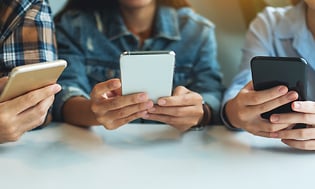 tre ungdommer bruker smarttelefon ved et bord