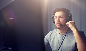 mann sitter foran dataskjerm og snakker i mikrofonenn på headsettet sitt