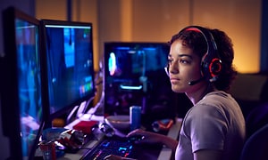 kvinne med gamer-headset foran tre dataskjermer