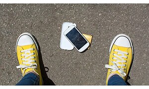 smarttelefon på asfalt med deksel av mellom gule sko