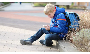 gutt sitter på fortau med smarttelefon i hånda