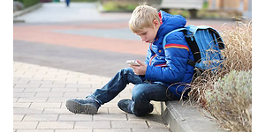 gutt sitter på fortau med smarttelefon i hånda