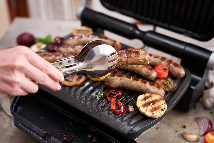 Mann griller pølser og grønnsaker på en elektrisk grill