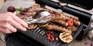 Mann griller pølser og grønnsaker på en elektrisk grill