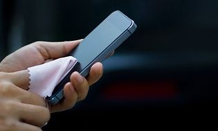 Person holder smarttelefon og rengjør skjermen med en pusseklut