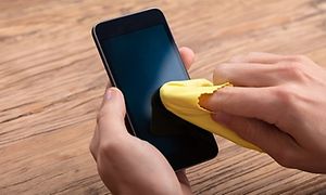 Person tørker av skjerm på smarttelefon med gul pusseklut