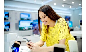 kvinne står i butikk smiler og ser ned på android-telefon