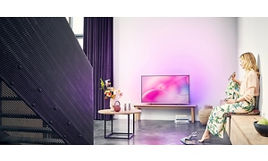 kvinne sitter foran tv-en og peker med fjernkontrollen mot den