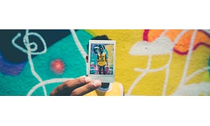 Mann foran fargerik vegg holder opp polaroid-bilde av seg selv