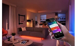 person holder smarttelefon og styrer smart belysning i stue via app
