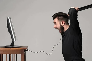 mann er sint på datamaskinen sin og har tastaturet klart til slag mot skjermen