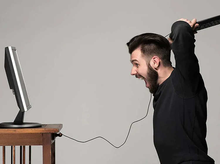 mann er sint på datamaskinen sin og har tastaturet klart til slag mot skjermen
