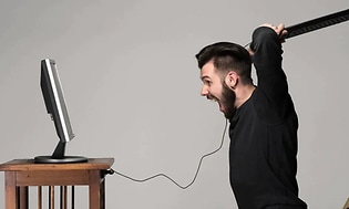 mann er sint på datamaskinen sin og har tastaturet klart til slag mot skjermen