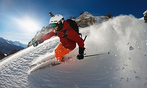 mann står på ski nedover bakke i strålende sol i puddersnø