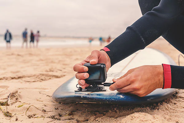 person monterer actionkamera på surfebrett på strand