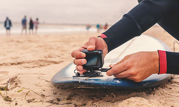 person monterer actionkamera på surfebrett på strand