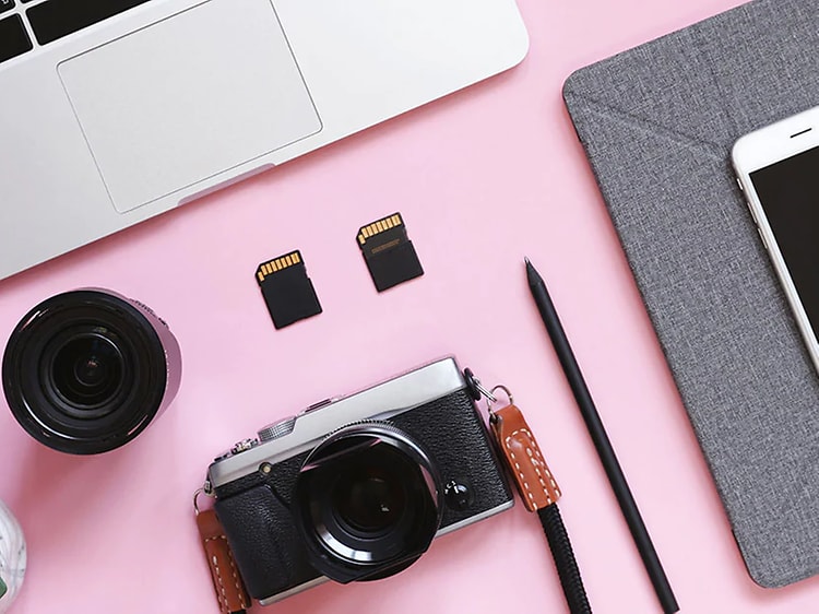 Kamera, objektiv, mac og smartelefon på et rosa bord