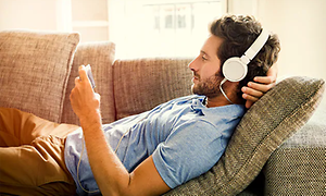 mann slapper av på sofa med headset og smarttelefon