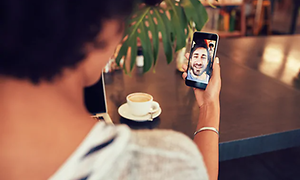 kvinne på kafé snakker i videosamtale med mann på smarttelefon