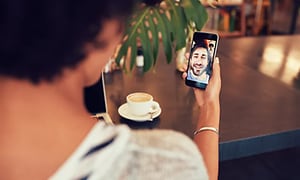 kvinne på kafé snakker i videosamtale med mann på smarttelefon 