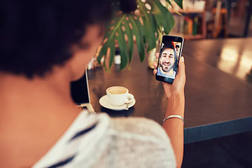 kvinne på kafé snakker i videosamtale med mann på smarttelefon 