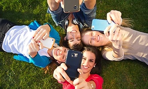 kvinner ligger på gress og smiler med smarttelefoner i hendene
